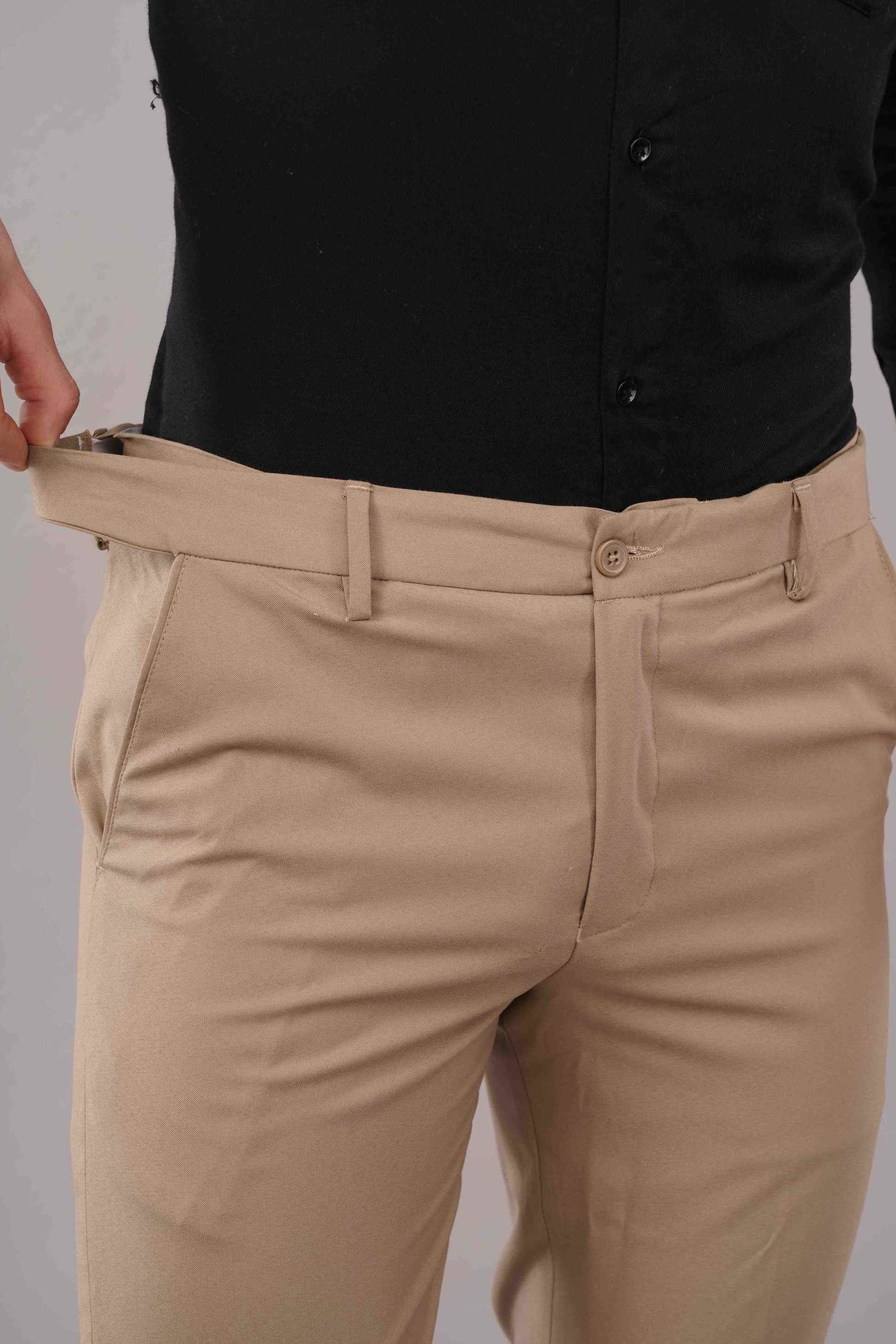 Beige pants being adjusted by a person wearing a black shirt against a neutral background