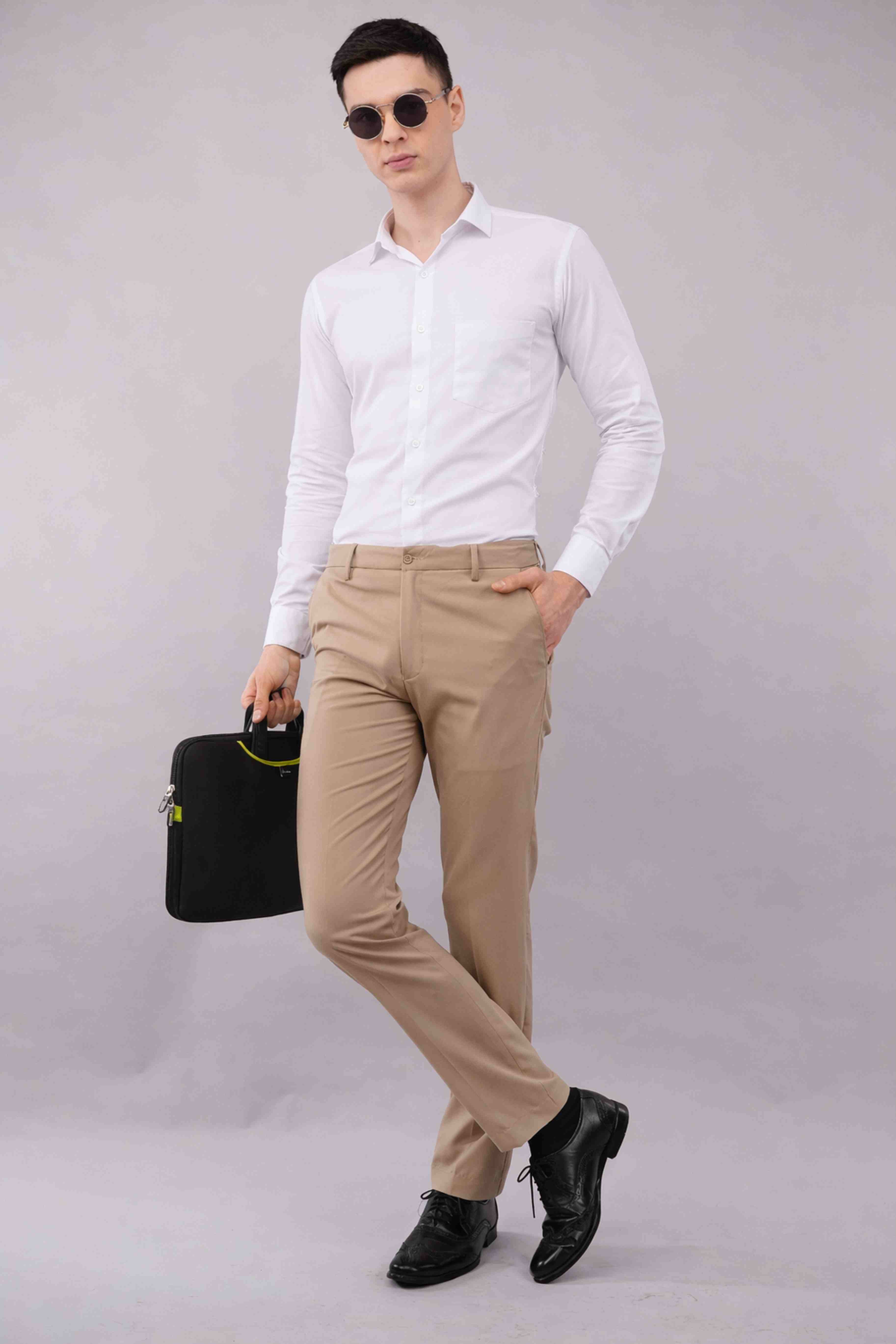 Man wearing a white shirt, stretchable beige pants, and black shoes holding a black bag